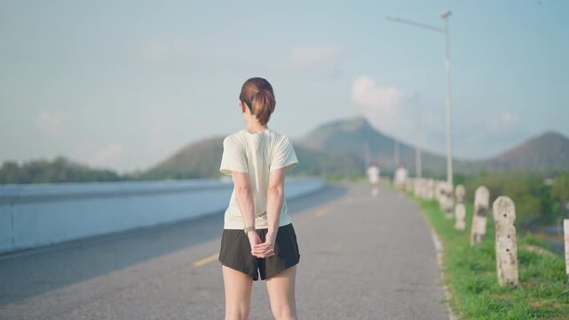 Young Asian woman warming up and stretching her muscles before jogging in the park. Female athlete getting ready for running workout in morning. Fitness, wellness and work life balance concepts