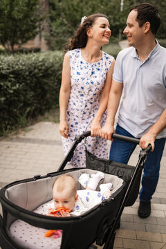 Happy parent talking and pushing infant baby stroller and walking in the park