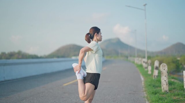 Young Asian woman warming up and stretching her muscles before jogging in the park. Female athlete getting ready for running workout in morning. Fitness, wellness and work life balance concepts