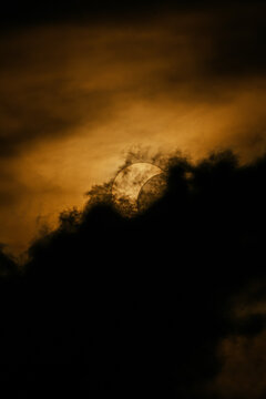 Solar eclipse behind dark cloud in dramatic amber sky