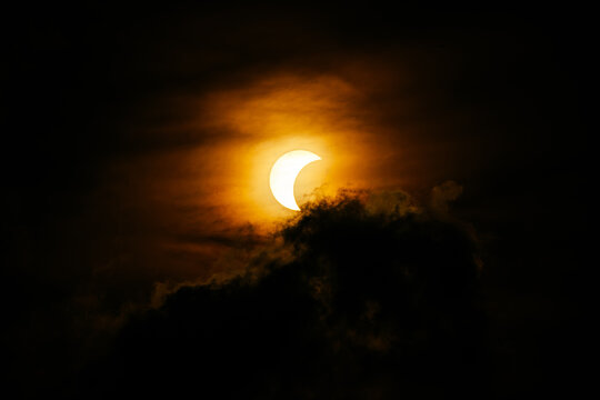 Partial solar eclipse glowing through dark dramatic cloud