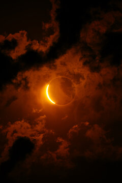 Solar eclipse with glowing crescent amid fiery clouds