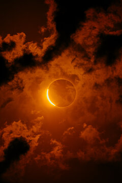Solar eclipse over fiery cloudscape with glowing crescent