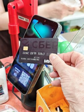 Kirov, Russia - May 5, 2026: Shopper hand holding a bank card near a contactless payment terminal at a supermarket checkout counter at 16:17
