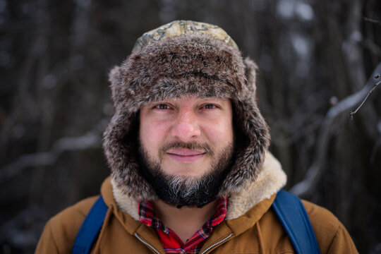 Bearded man in fur trapper hat in winter forest