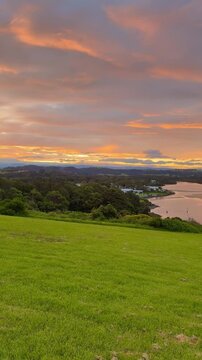 A girl stands on the grassy meadow admiring a stunning orange sunset over the bay at Minnamurra Lookout, near Jervis Bay, Wollongong and Kiama, New South Wales, Australia.
