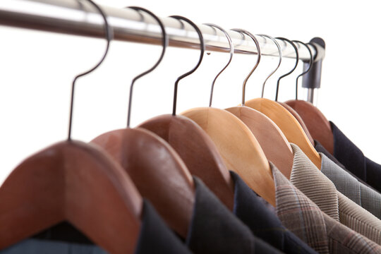 Low angle close up of men suit jackets and blazers hanging on wooden hangers on metal rack against white background.