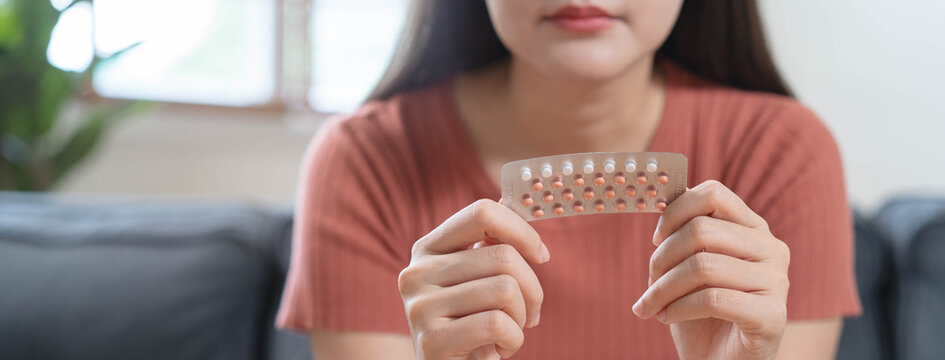 Close up woman holding oral contraceptive birth control pills blister pack and a glass of water, concept of unwanted pregnancy prevention and female healthcare.