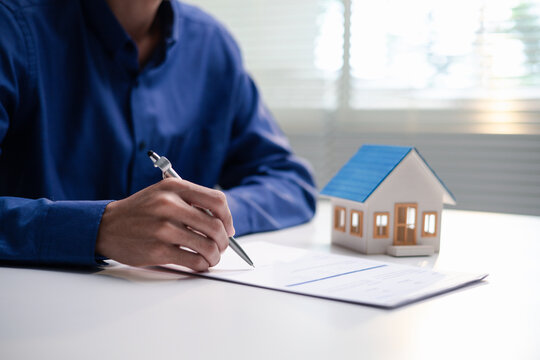 Insurance agent reviews a home insurance application at an office desk. A model house and policy documents represent property coverage, risk assessment and financial protection for homeowners.