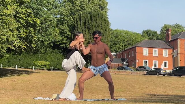 Couple practicing acro yoga on sunny lawn outside historic hotel in Kent, England