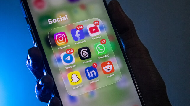 Close up of smartphone screen displaying social media application icons in folder with blue backlighting.
