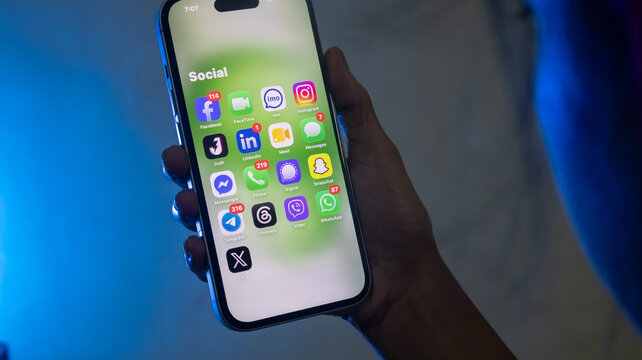 Person holding iPhone displaying popular social media apps folder on green screen.
