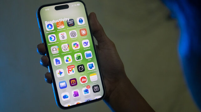 Person holding iPhone displaying various productivity and workspace application icons on green screen.