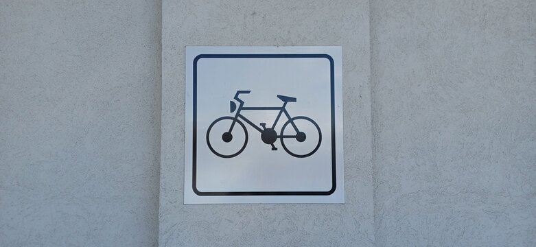 Quadratisches Hinweisschild mit schwarzem Fahrrad-Piktogramm an einer hellen Verputzwand