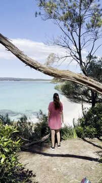 A girl in a pink dress admires the turquoise ocean and white sand at wild Chinamans Beach, on the White Sands Walk near Greenfield Beach, Jervis Bay, New South Wales, Australia.