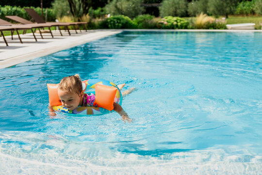 Little girl with armbands and floaty swimming in pool