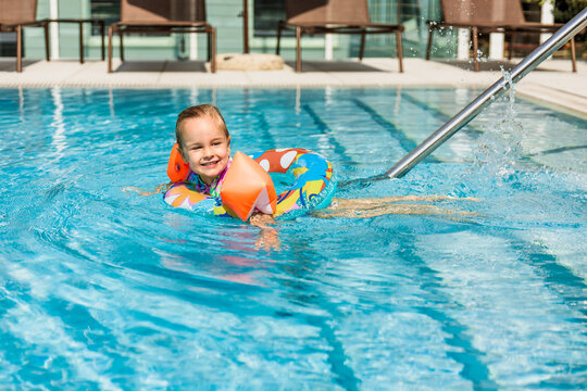 Happy young girl with floaties swims in a pool