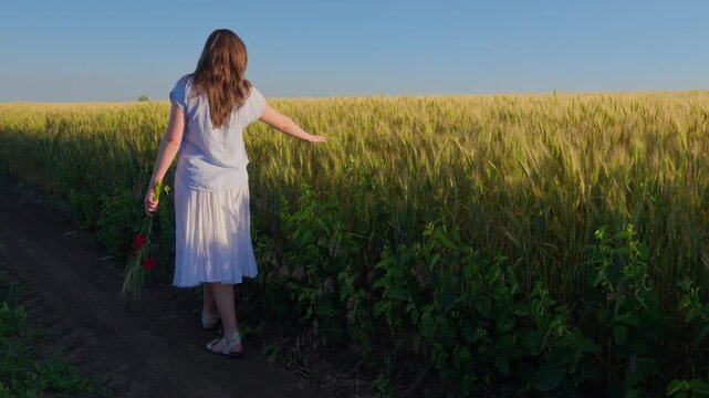 A beautiful young teenager girl in white dress walking along the edge of a ripe wheat field during golden hour, feeling free and peaceful in the countryside landscape
