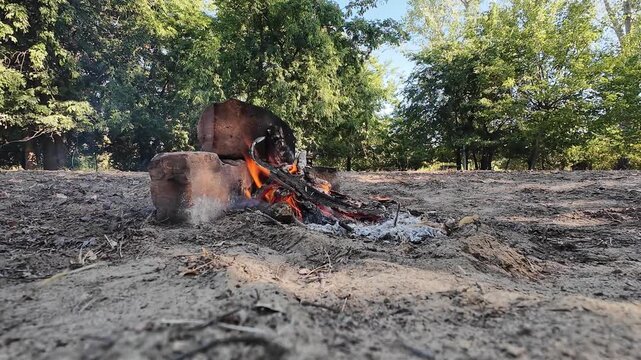 Kleines Lagerfeuer mit brennendem Holz und Ziegelsteinen auf sandigem Boden in der Natur