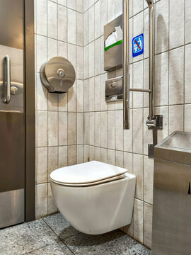 Handicapped accessible toilet with grab bar support in public restroom. Disabled bathroom facility with stainless steel fixtures and ADA compliant equipment for medical assistance