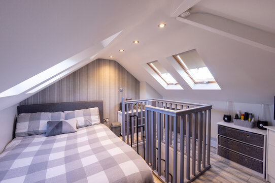 Converted loft bedroom with double bed sloping white ceilings roof windows recessed lighting grey striped feature wall wooden flooring and open stairwell with painted balustrade