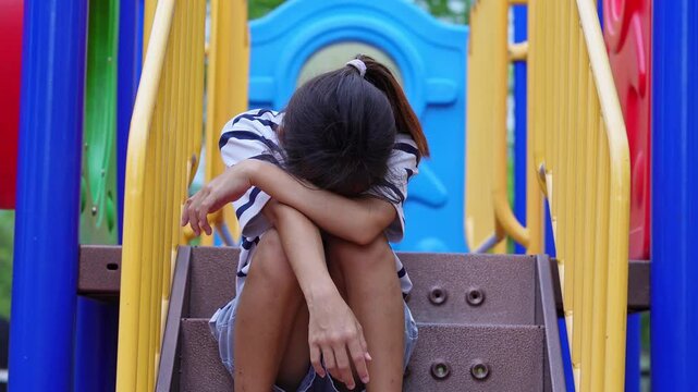 Sad upset Asian girl sitting alone with head down on playground stairs feeling lonely
