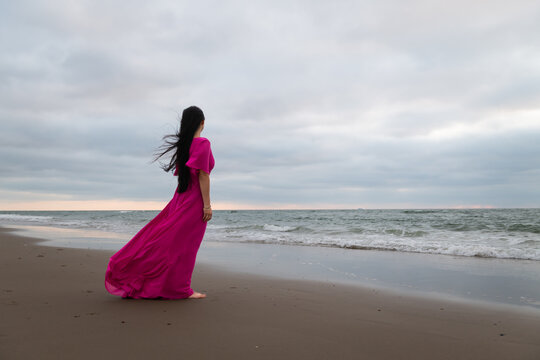 anonymous young woman in classic long pink dress walking on the beach