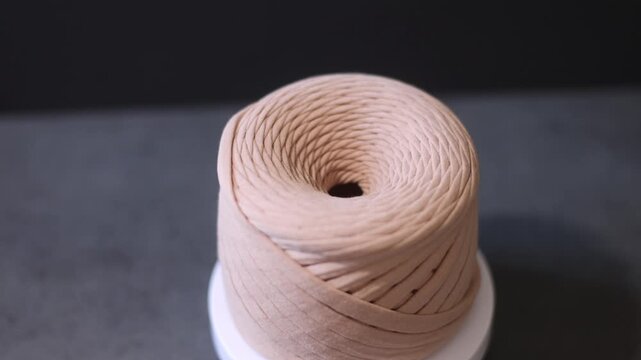 Cream-colored yarn spool with trailing thread, knitting accessory.
