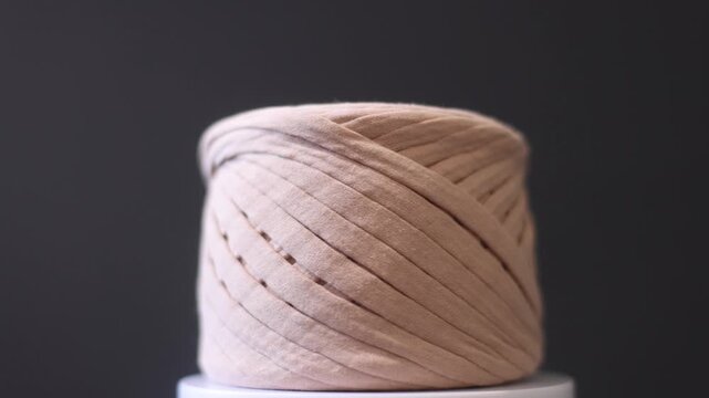 Cream-colored yarn spool with trailing thread, knitting accessory.
