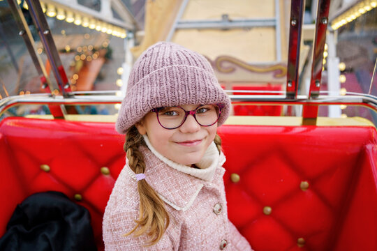 Little school girl riding on ferris wheel on Christmas market. Happy child in winter clothes.