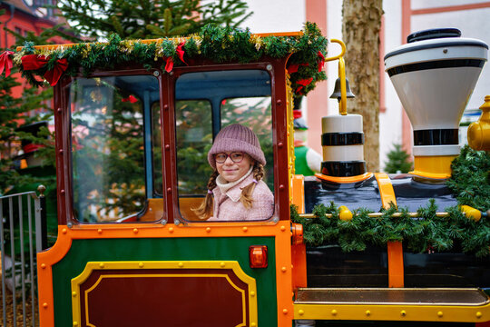 Little school girl on a carousel train at Christmas funfair or market, outdoors. Happy child having fun. Traditional xmas market in Germany, Europe. Holiday, children, lifestyle concept