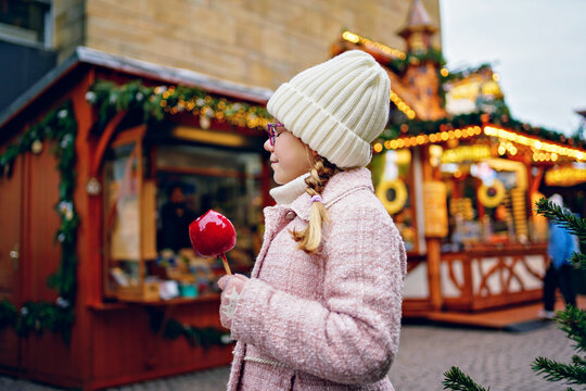 Little cute kid girl eat sweet sugar covered red candy apple on Christmas market. Happy child on traditional Xmas fair in Germany.