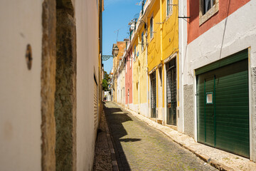 Fototapeta premium Colorful residential facades and a green garage door line a narrow cobblestone alley in Lisbon, Portugal.
