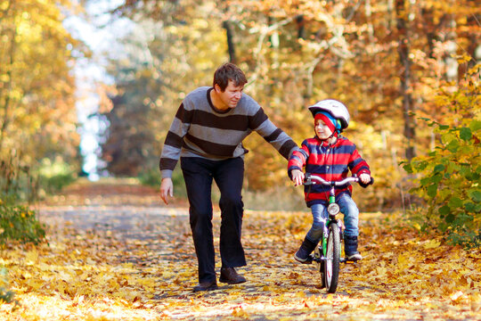 Little kid boy and his father in autumn park with a bicycle. Dad teaching his son biking