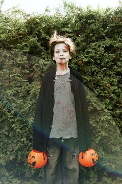 Portrait of Caucasian male teenager wearing zombie Halloween makeup holding pumpkin candy buckets outdoors. Image usable for seasonal holiday advertising, vertical