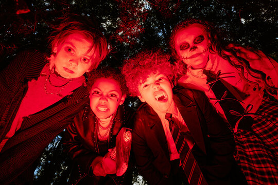 Portrait of diverse multiethnic group of children wearing scary Halloween makeup and costumes posing outdoors, low angle shot. Concept for holiday party marketing and seasonal promotion