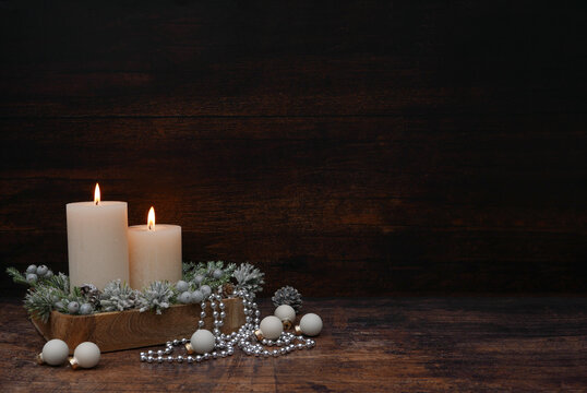 Atmospheric Christmas arrangement with lit candles on a dark, rustic wooden background, with plenty of space for text.