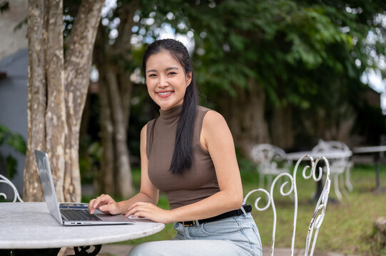 Happy Asian Woman Typing On Laptop At Outdoor Garden Table