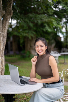 Smiling Asian Woman With Laptop Looking At Camera Outdoors