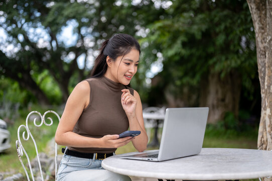 Happy Asian Woman Looking At Laptop Screen Holding Smartphone