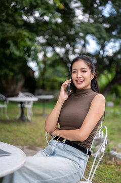 Asian Businesswoman Talking On Mobile Phone In Garden Cafe