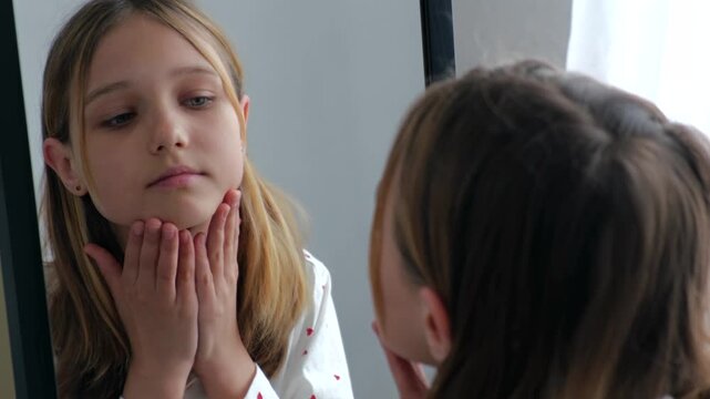 Teenage girl closely examines her face in a mirror with a critical, concerned expression. Concept of self-image, appearance insecurity, low self-esteem, and adolescent psychological issues.