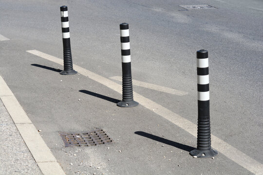 A high angle shot of three flexible black plastic traffic delineator bollards with reflective white stripes installed on an asphalt road surface.