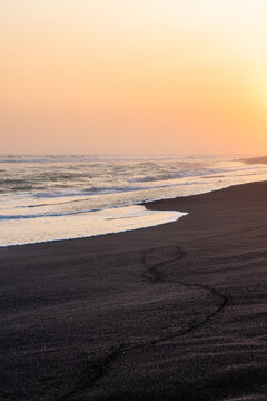 Ocean waves crashing on dark sand shore during golden sunset