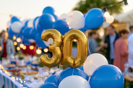 Golden number thirty balloon surrounded by blue and white balloons at outdoor party table with string lights and guests mingling during late afternoon light