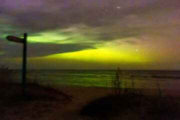 Aurora Borealis above a dark beach landscape with stars and colorful night sky, creating a dramatic natural light display over the sea. © Anna