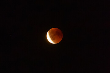 Blood moon during a lunar eclipse glowing red and orange against a dark night sky, dramatic astronomical event and celestial phenomenon. © Anna