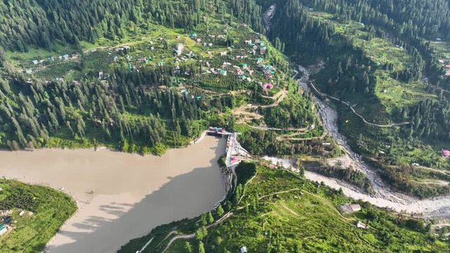 High angle drone tracking shot over the Parbati-2 HEP Dam and sediment-heavy reservoir in Barshaini, a key energy infrastructure site in Parvati Valley, Himachal Pradesh.