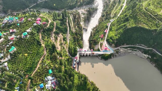 Aerial top-down view of the concrete spillway discharging water into the river near Barshaini village, highlighting hydroelectric power generation in Kullu District, India.