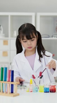 Asian Schoolgirl Performing Science Experiment with Colorful Liquids in Laboratory